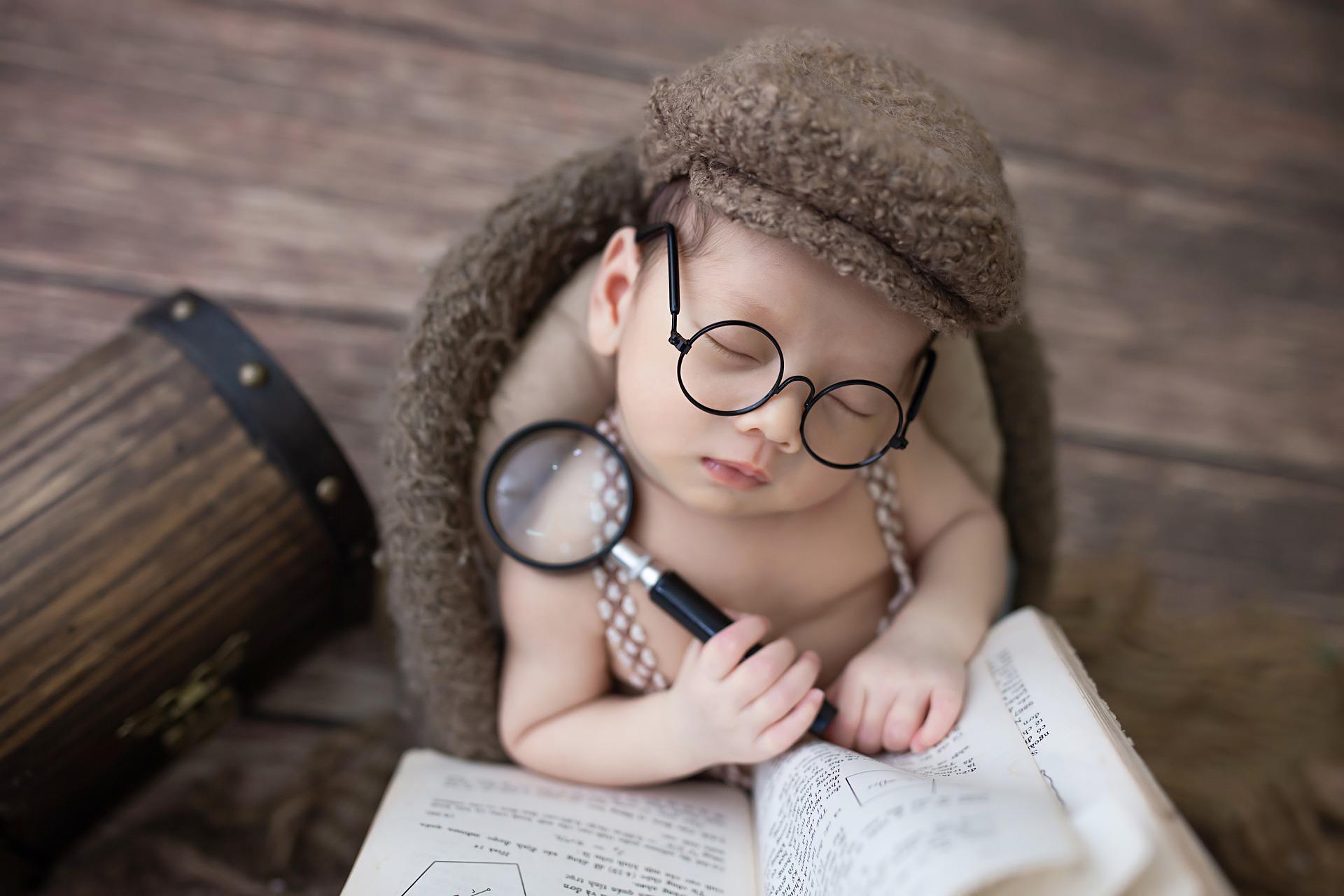 kleiner schlafender Junge mit Brille und Lupe in der Hand vor einem Buch